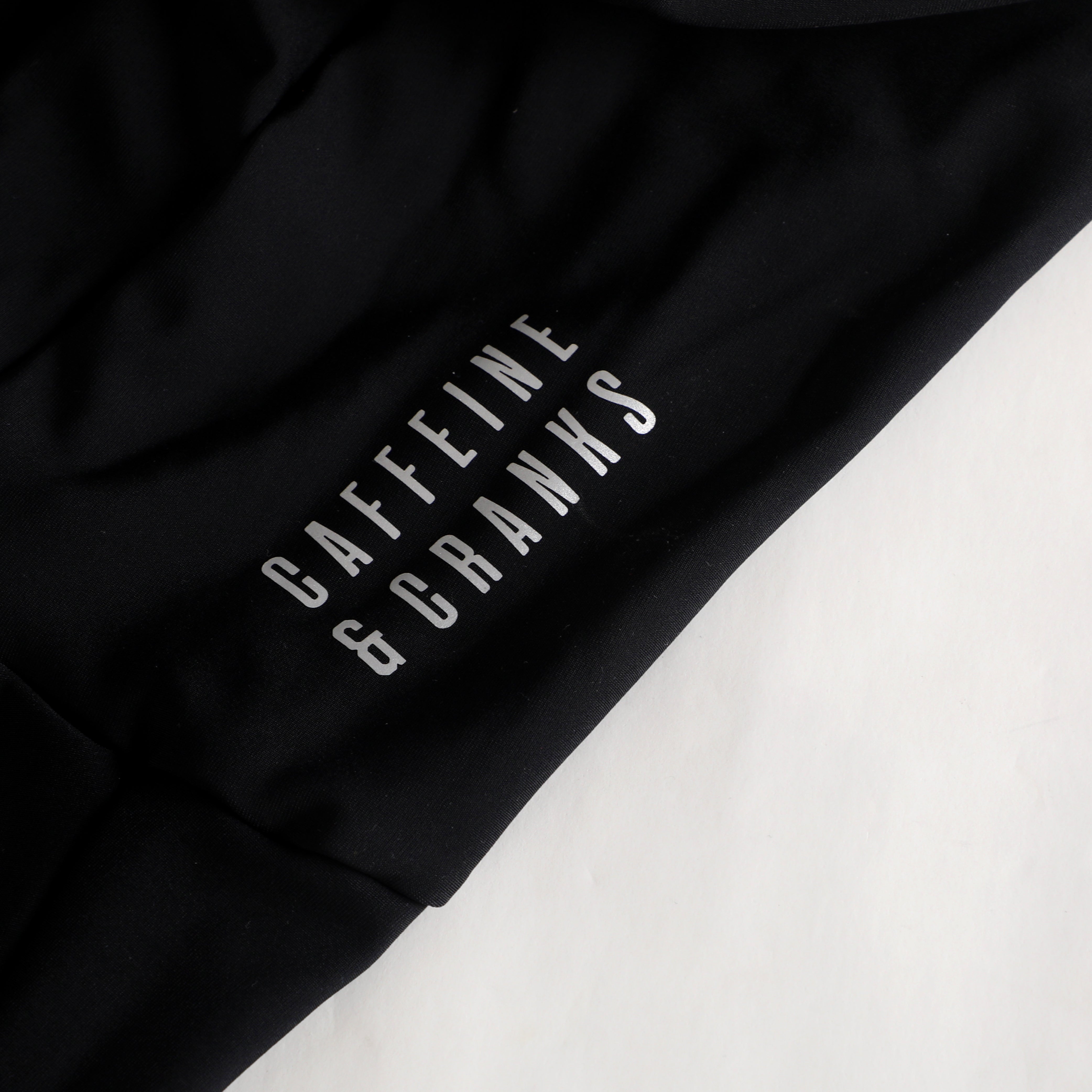 Close-up of black thermal bib with silver 'CAFFEINE & CRANKS' logo on sleeve.