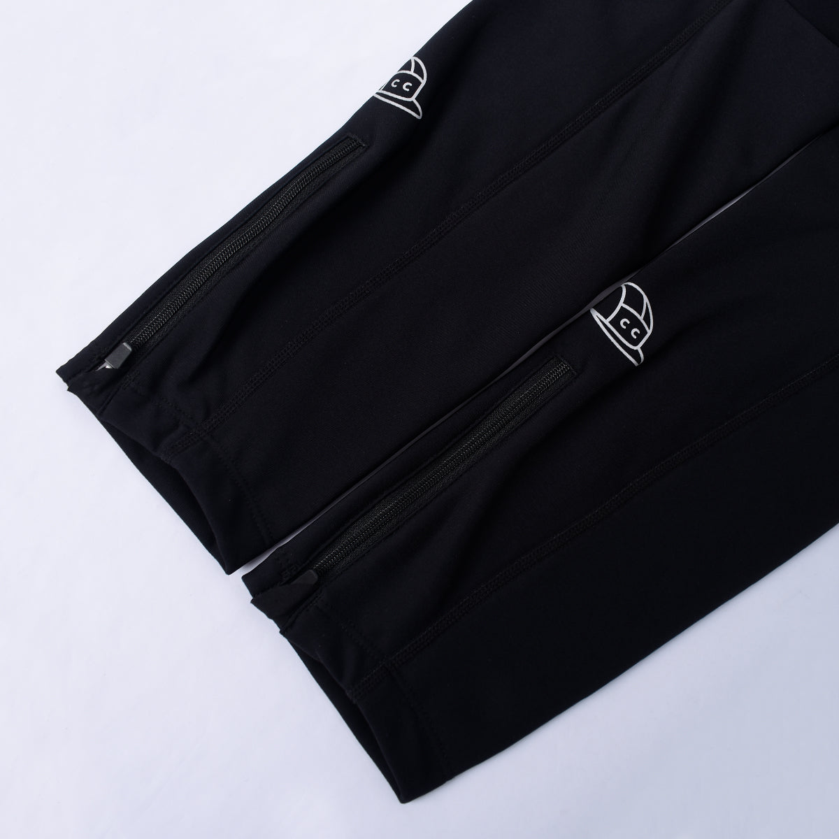 Close view of black thermal leg warmers with white logo and zippered ankles.