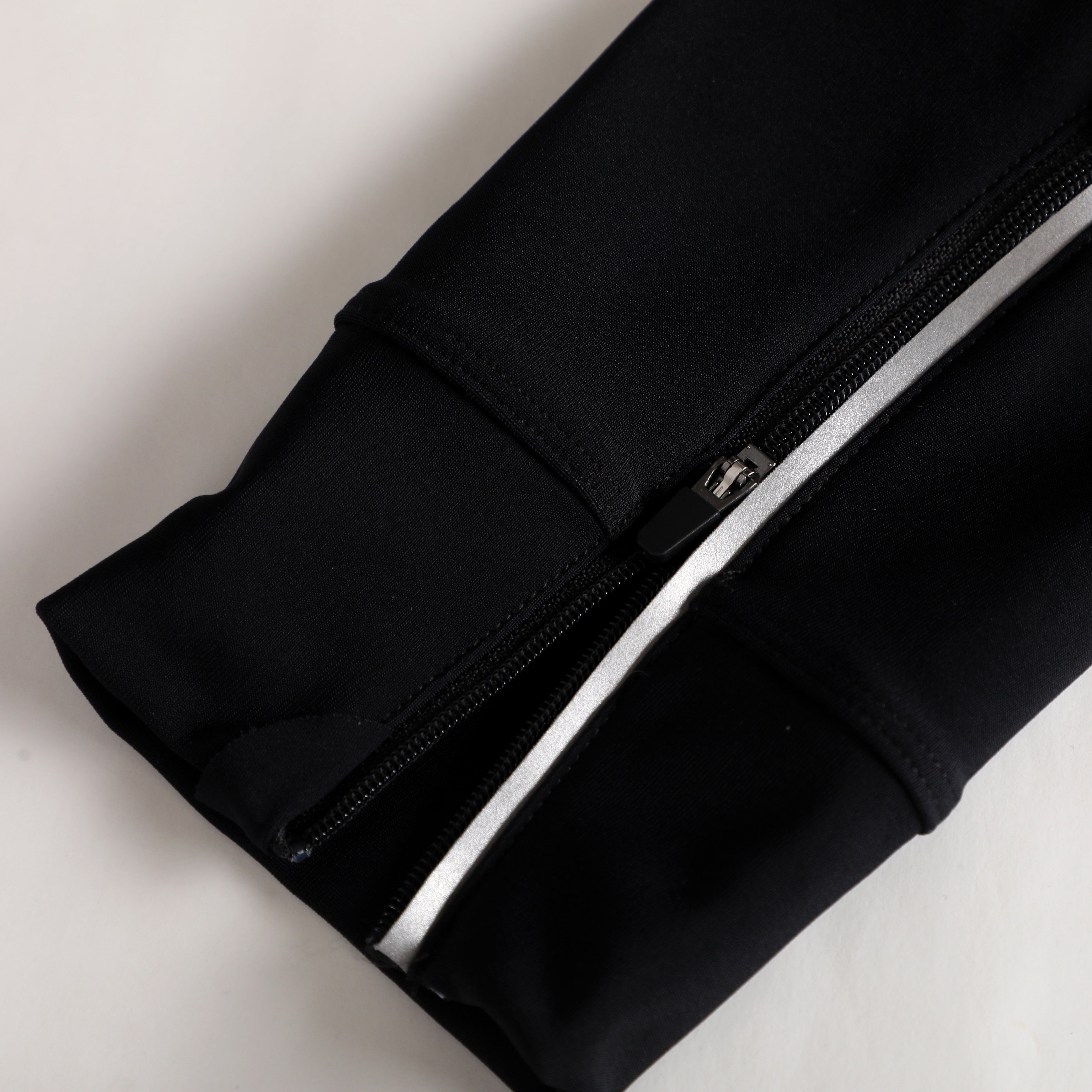 Close-up on black thermal bib with silver reflective stripe and zipper detail.