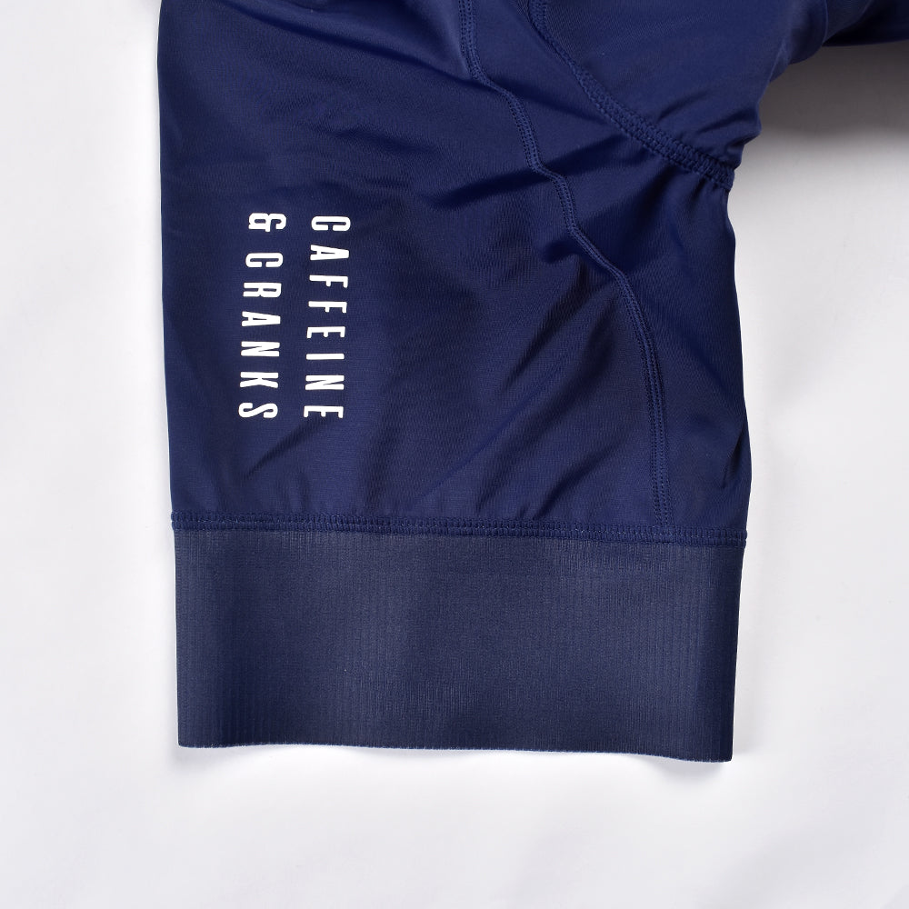 Close-up of navy women's bib shorts with white "CAFFEINE & CRANKS" logo and ribbed hem.