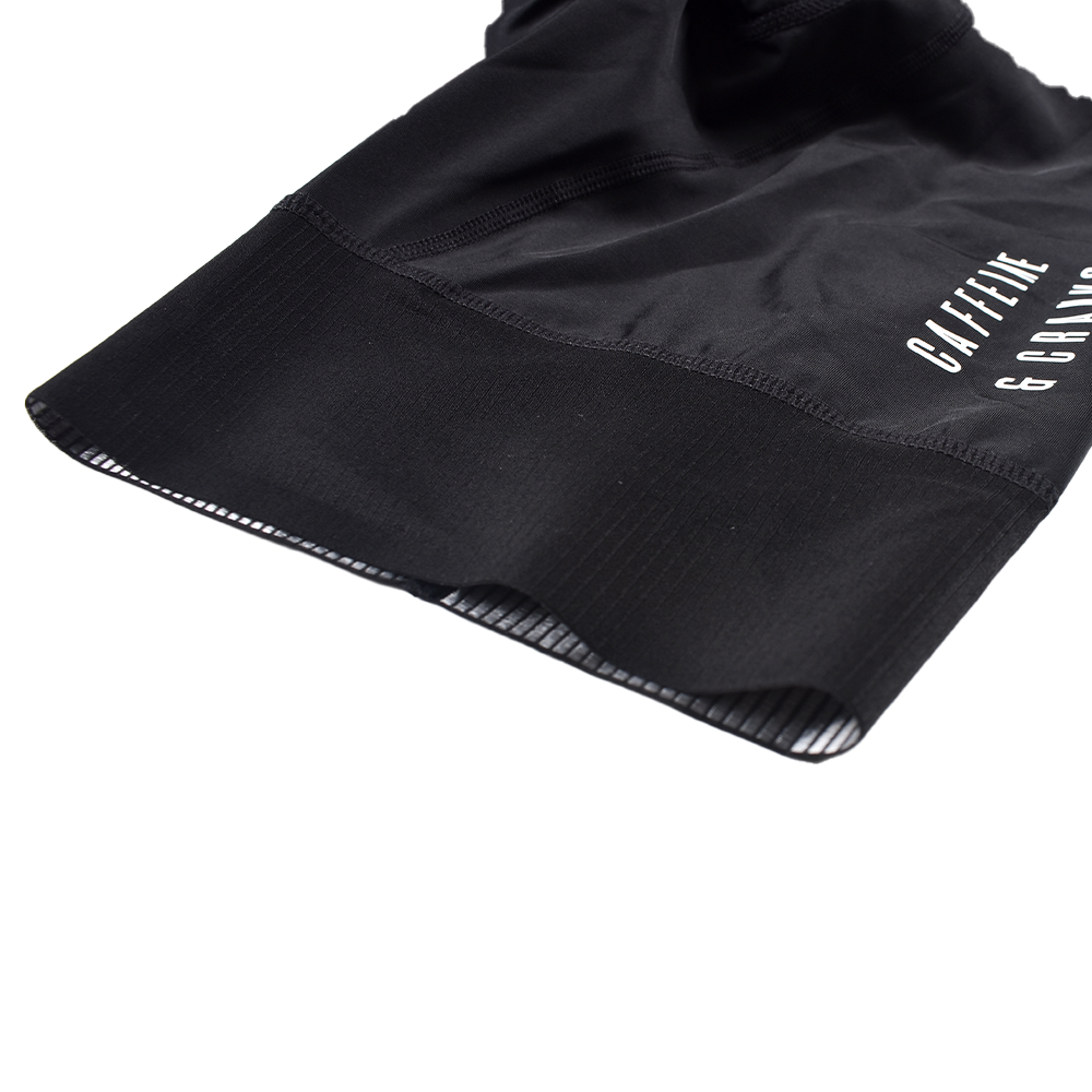 Close-up of black men's Core Bib Shorts leg hem with white logo detail