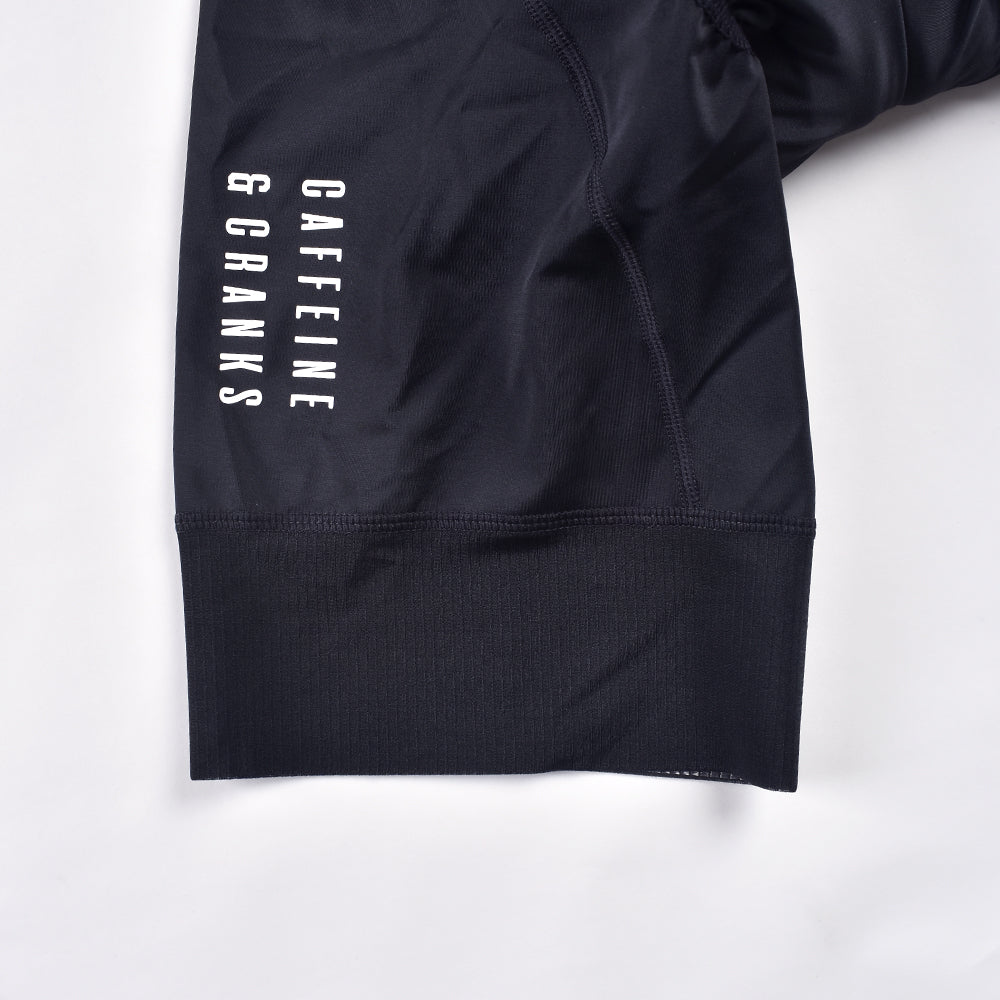 Close-up of black women's bib shorts with white "Caffeine & Cranks" logo and ribbed hem.