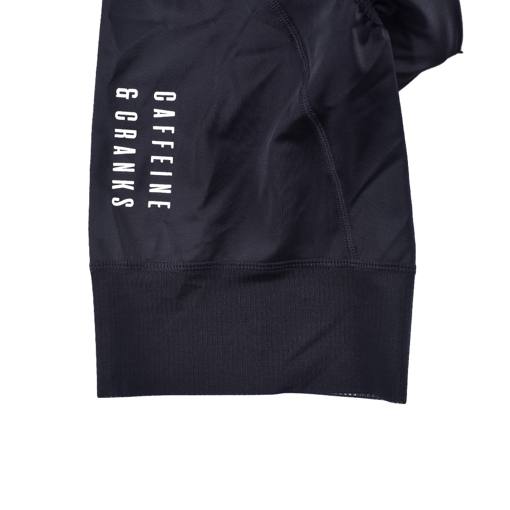 Close-up of black men's bib shorts with white "CAFFEINE & CRANKS" logo on leg.