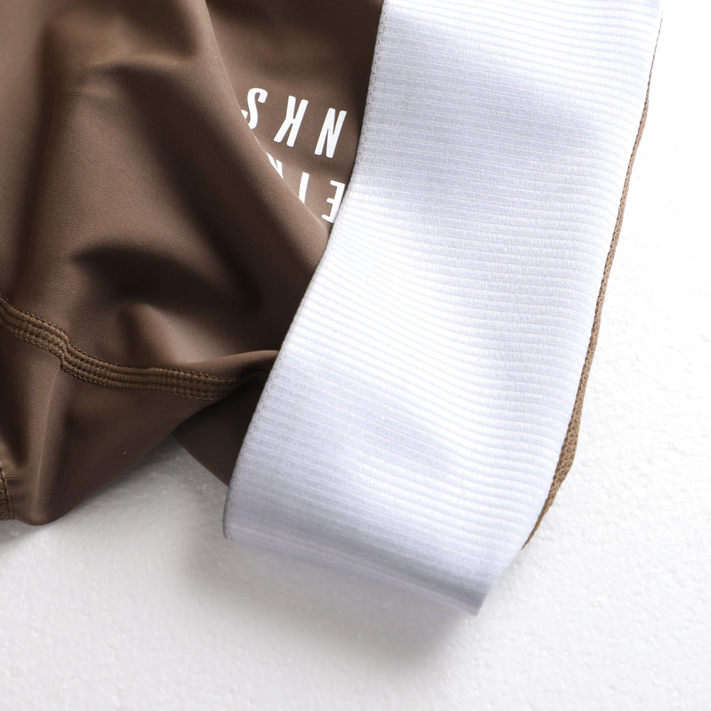 Close-up of women's mocha bib shorts with white elastic leg opening and subtle branding.