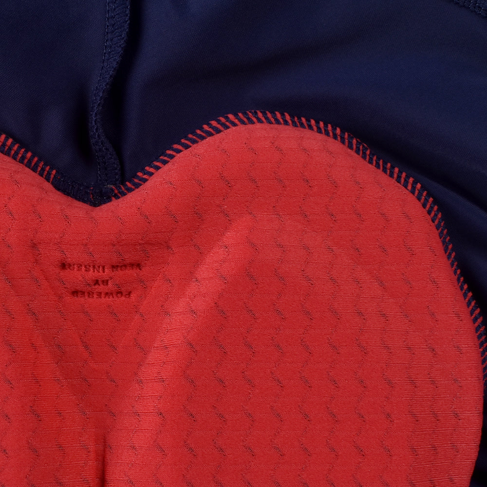 Closeup of navy bib shorts with red padded insert featuring textured pattern and "Powered by" text.