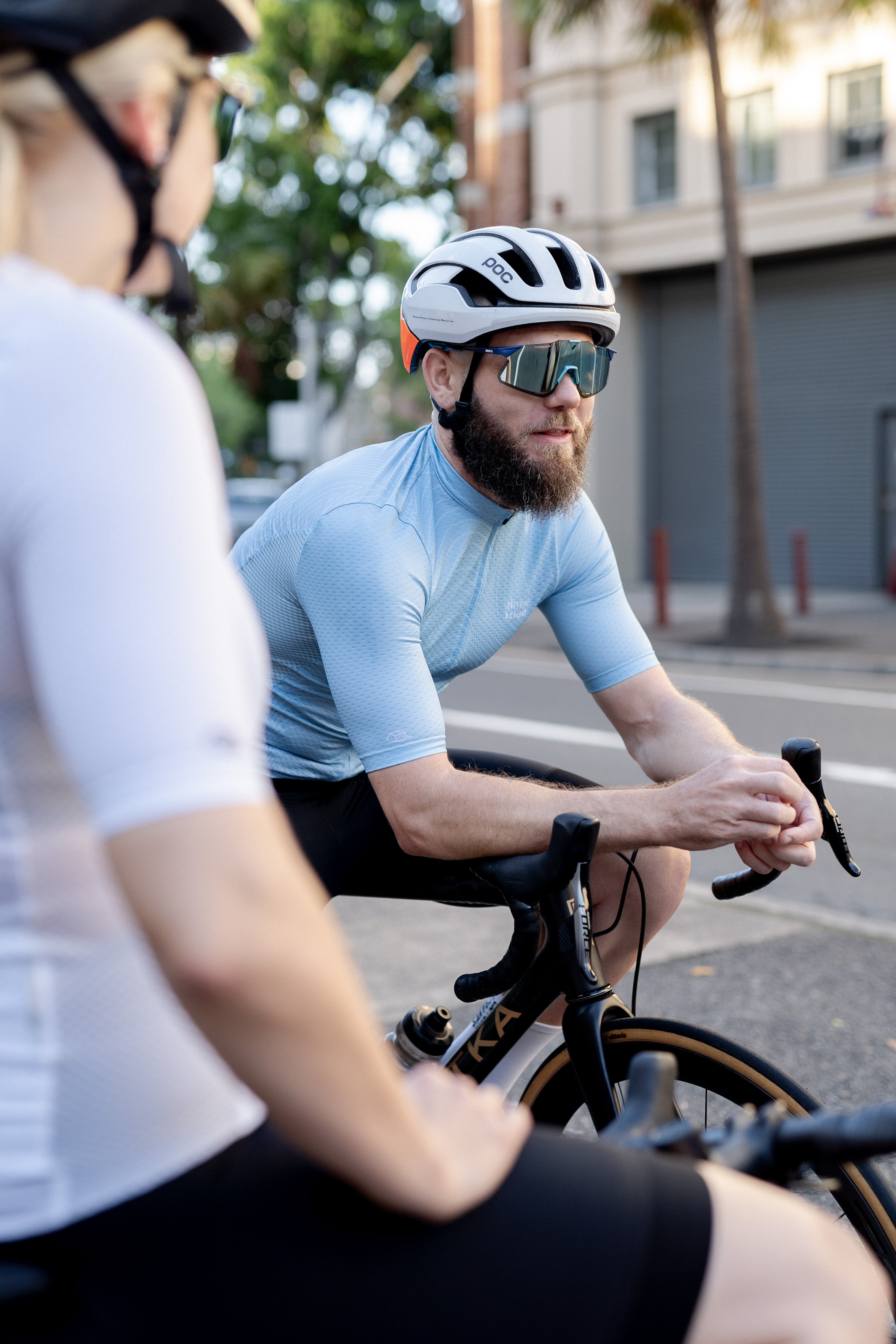 Man in light blue C&C Cerulean Topo Jersey, black shorts, white helmet, and mirrored sunglasses.