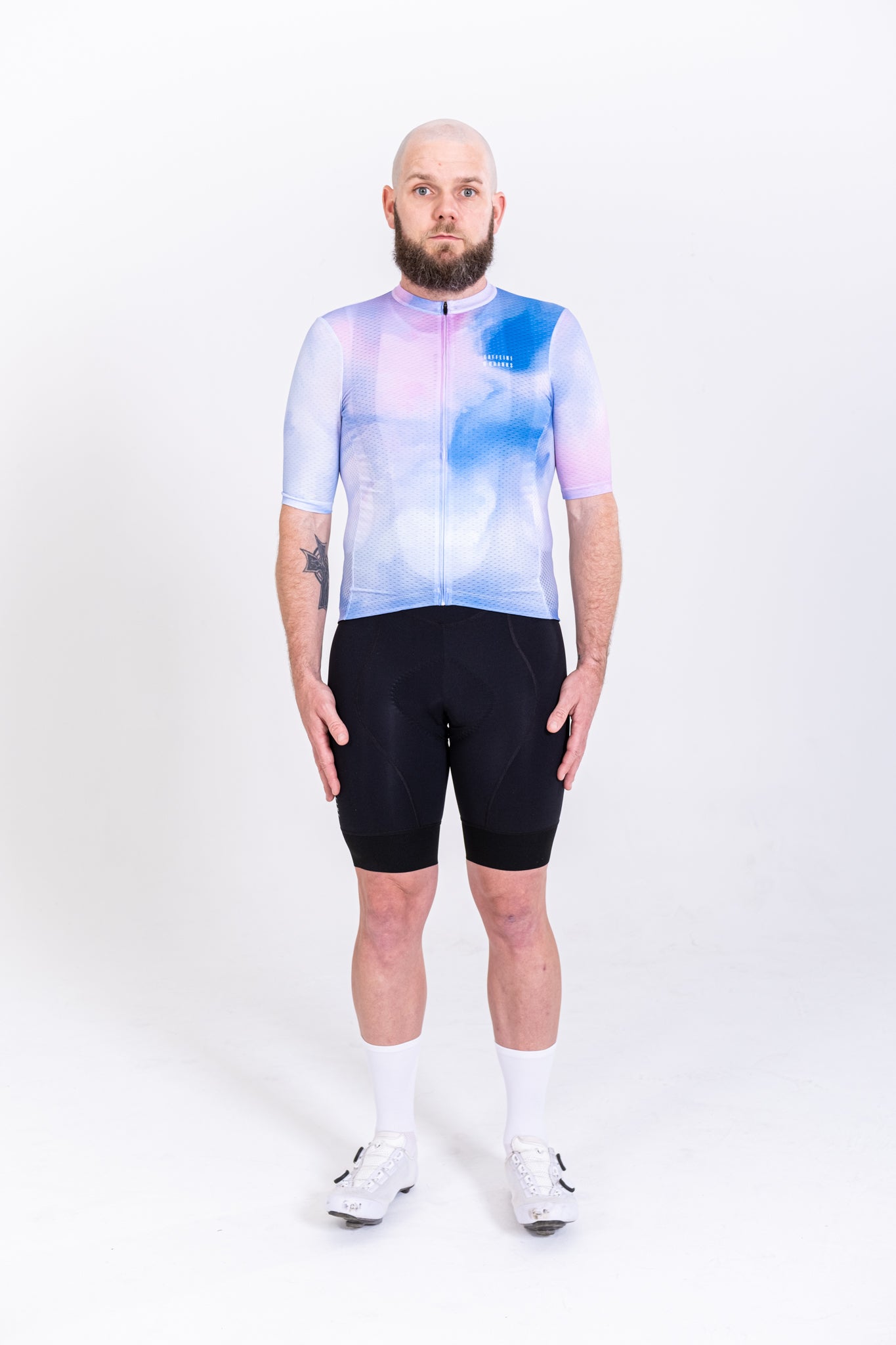 Mens jersey with a coral, blue, and pink abstract pattern, black cycling shorts, and white socks.