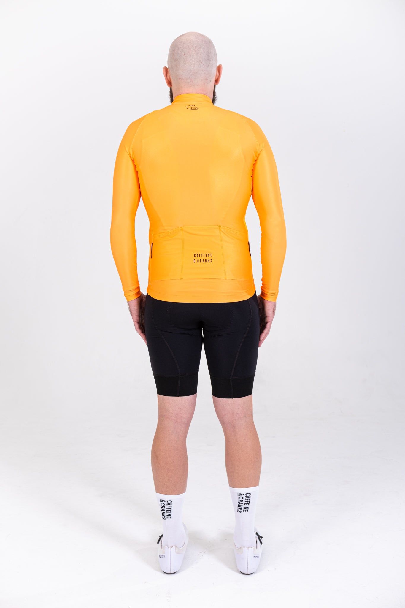 Back view of a man wearing an orange long-sleeve thermal jersey and black cycling shorts.
