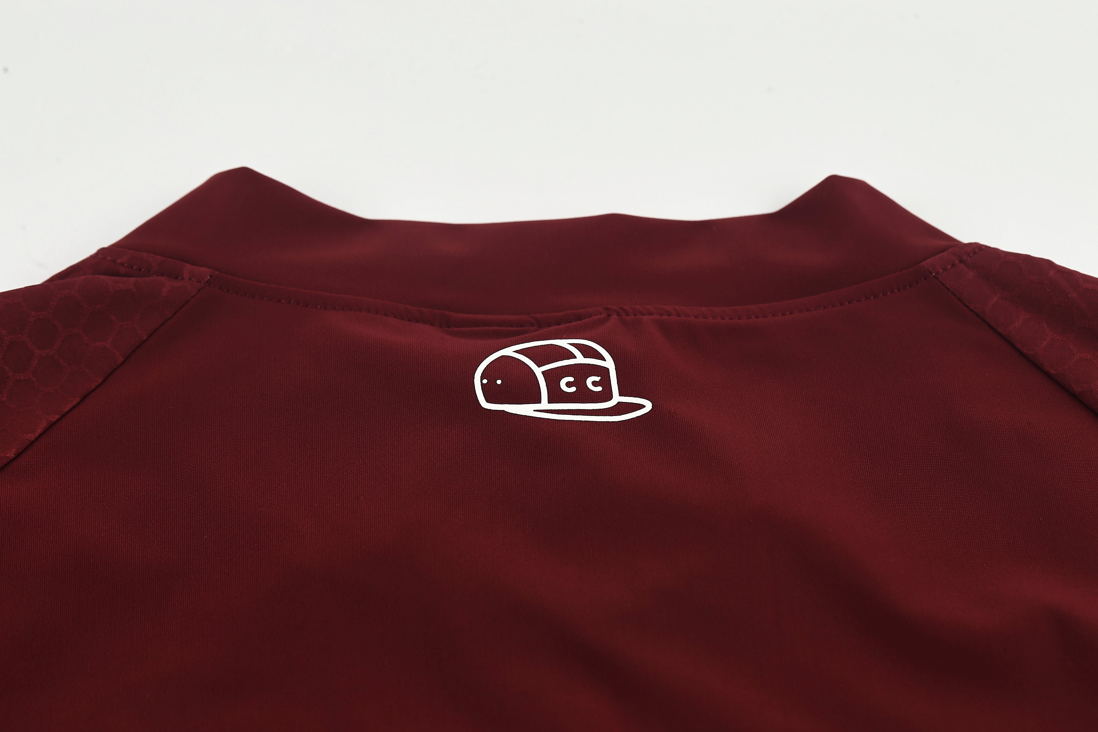 Back detail of a wine-colored women's Pinnacle Jersey with a white outline logo of a cap.