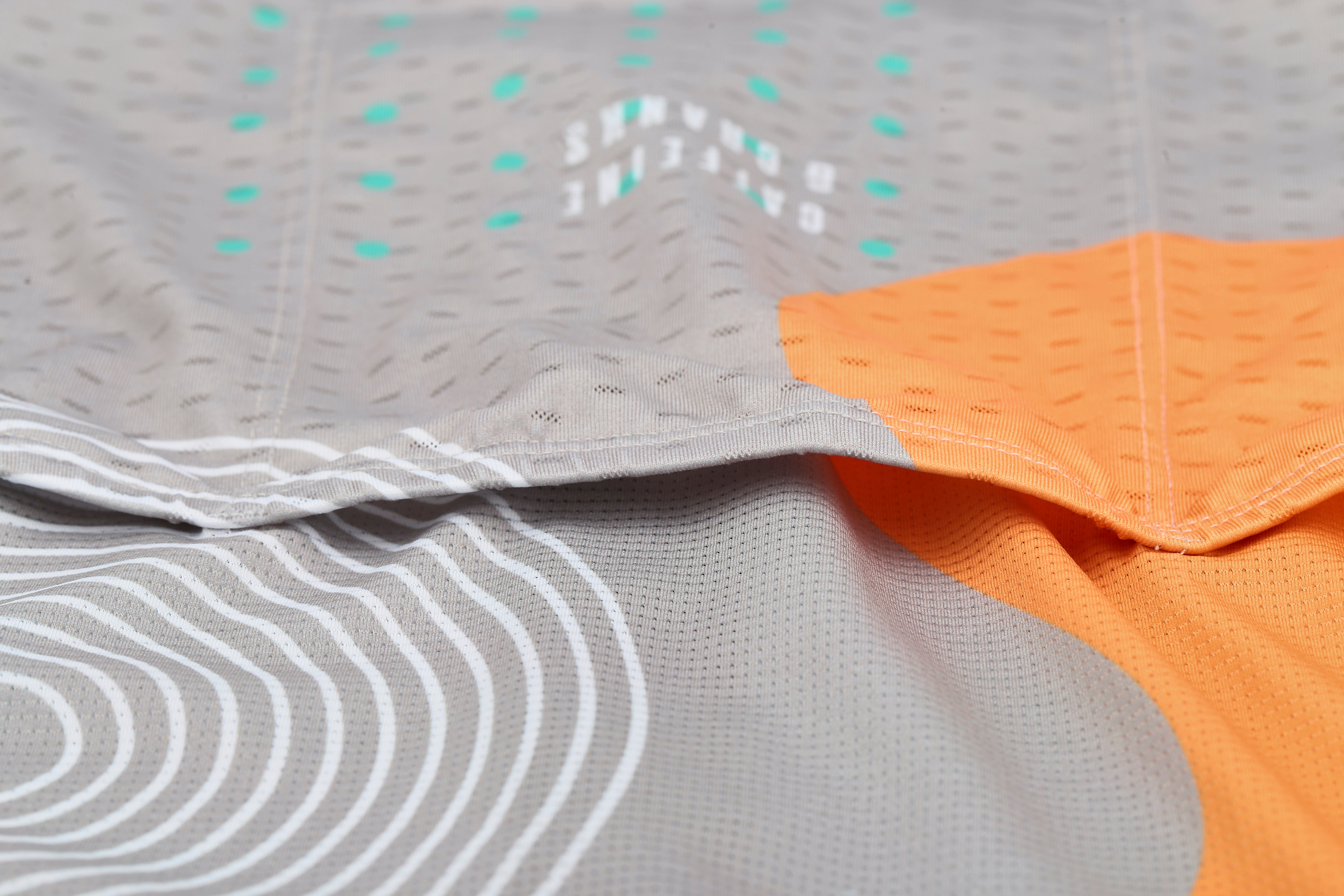 Close-up of C&C Memphis Light Jersey: grey fabric with white lines, orange panel, and teal dots.