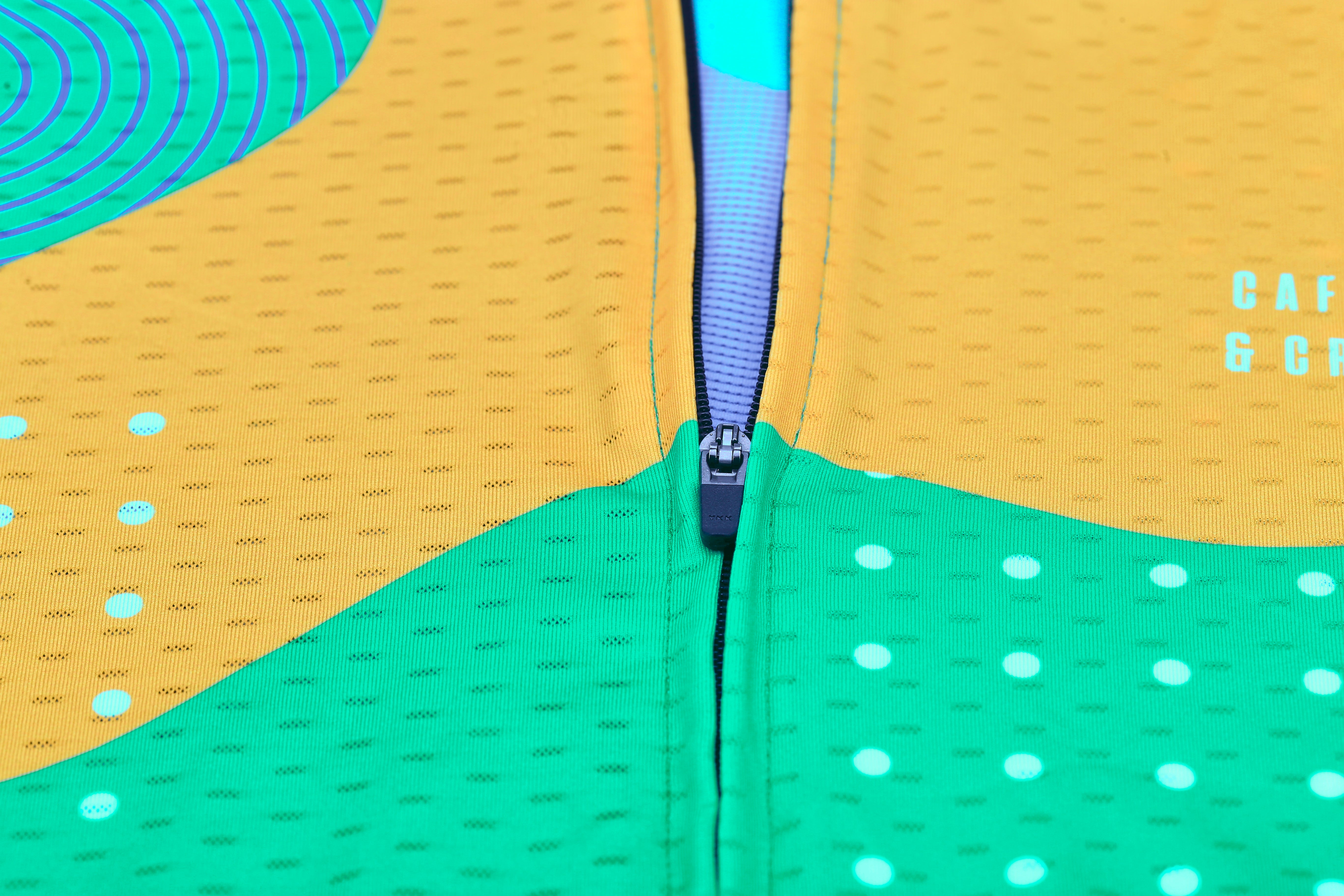 Close-up of C&C Memphis jersey zipper with green, yellow, and blue abstract patterns.