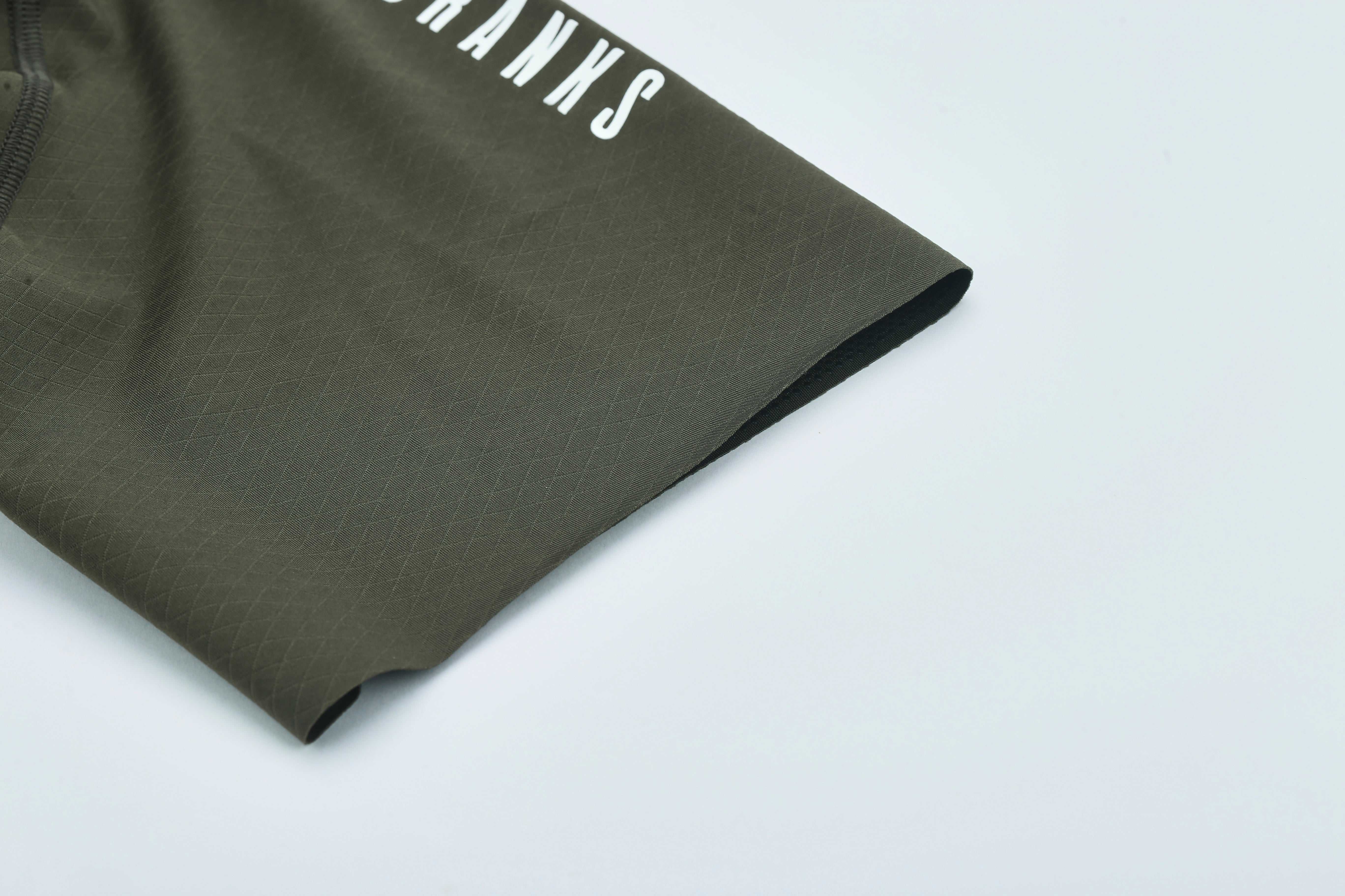 Close-up of olive bib shorts cuff with diamond texture & white logo.