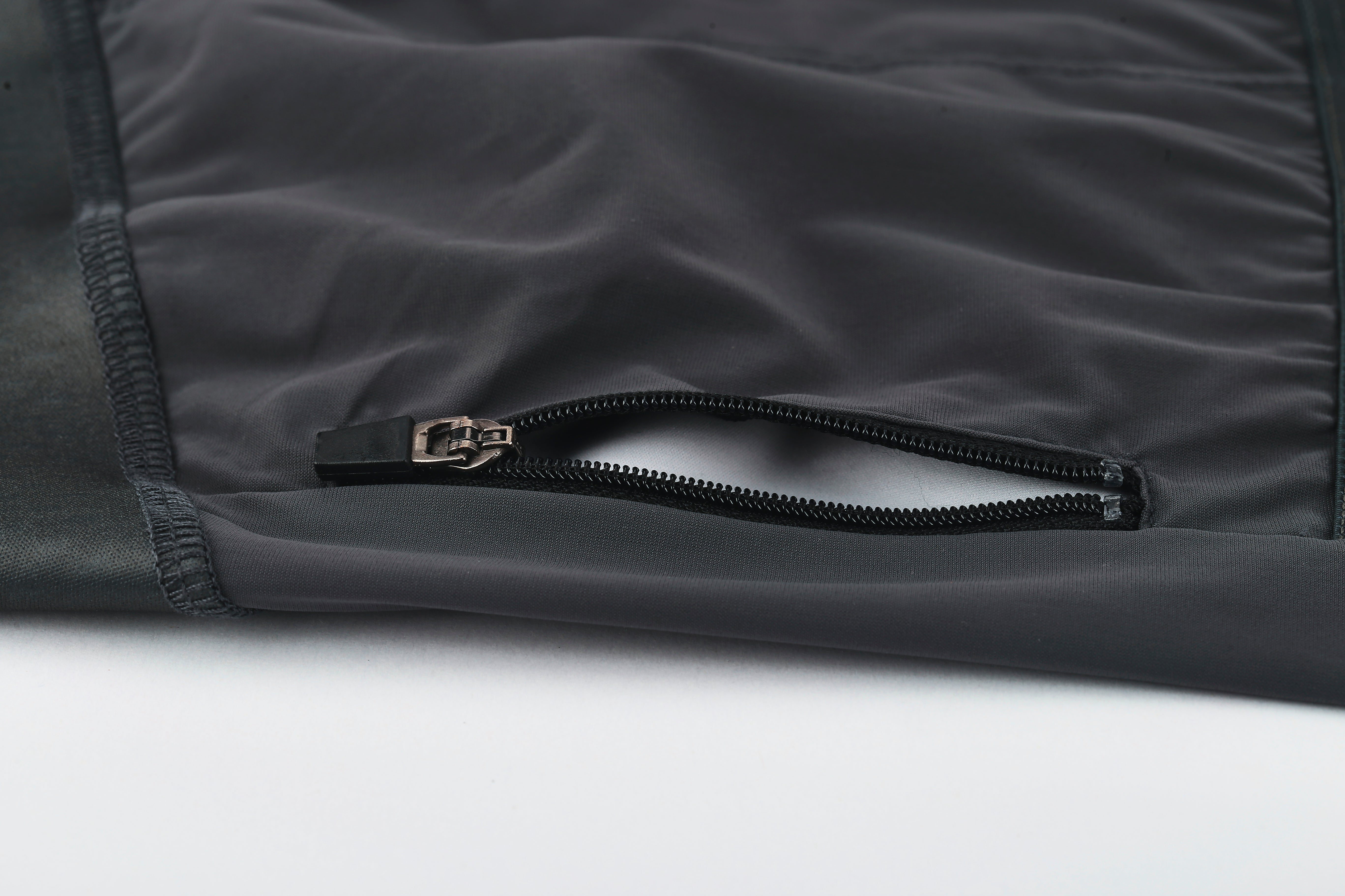 Close-up of the Pinnacle Jersey in slate grey, showing an open zipper pocket with a black zipper pull. Color: Slate grey.