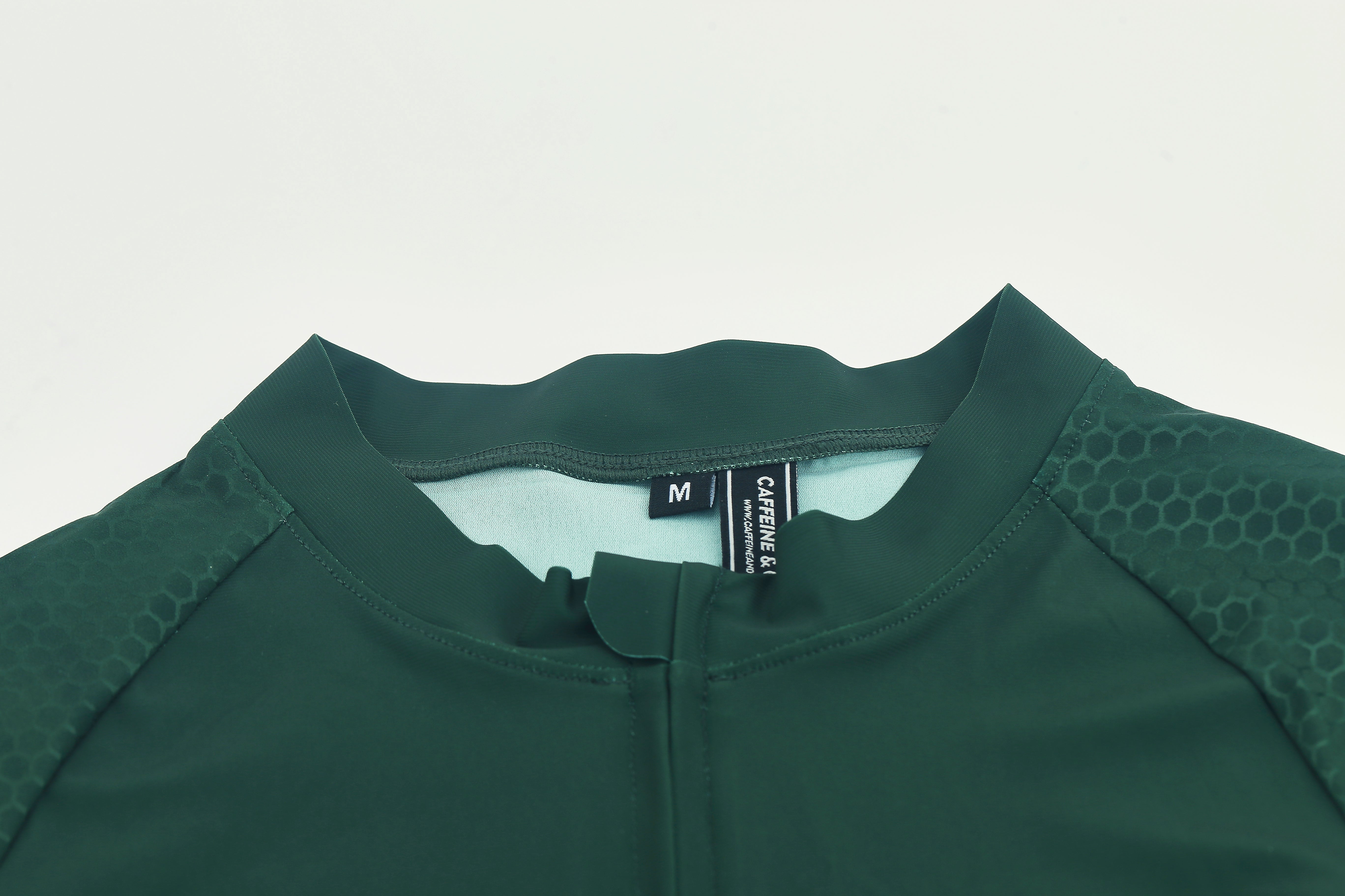 Close up of Pinnacle jersey featuring dark forest green fabric, hexagonal sleeve pattern, and size M tag.