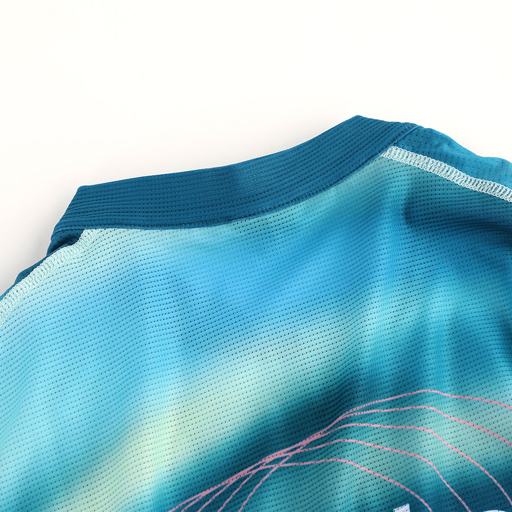 Close-up of C&C Flux Jersey collar and shoulder in teal & blue gradient with pink graphic detail.