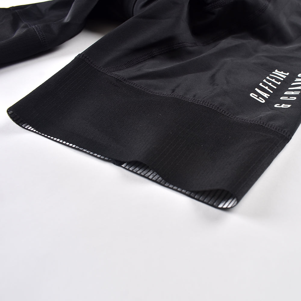 Close-up of black women's cycling bib shorts with silicone gripper on leg opening and white logo.