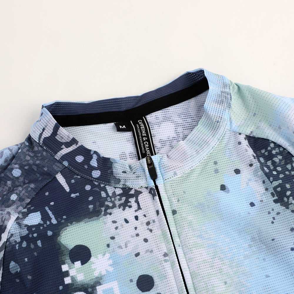 Close-up of a men's C&C jersey with an abstract overspray design in blue, green, and dark grey.