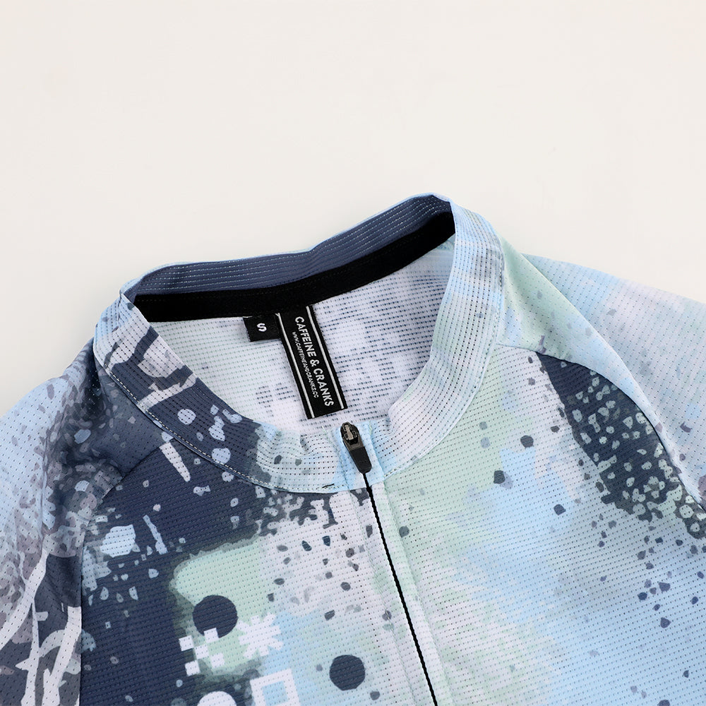 Close-up of C&C Overspray Jersey for women, featuring blue, white, and gray splatter print & full zip.