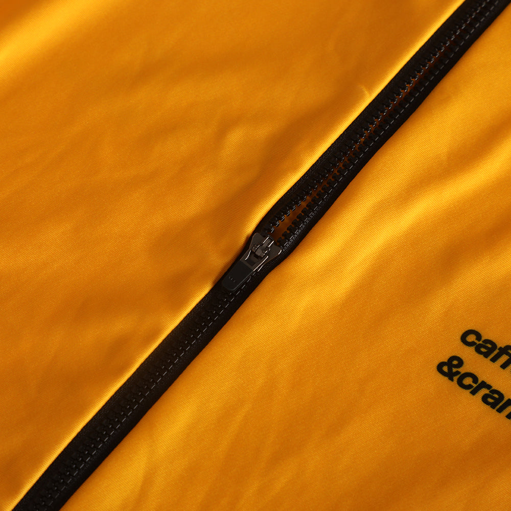 Close-up of a yellow women's thermal jersey with a black zipper and black text.