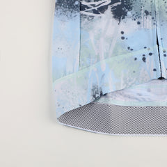 Close-up of the C&C Overspray Jersey hem showing a blue, green, and grey abstract print and dotted mesh trim.