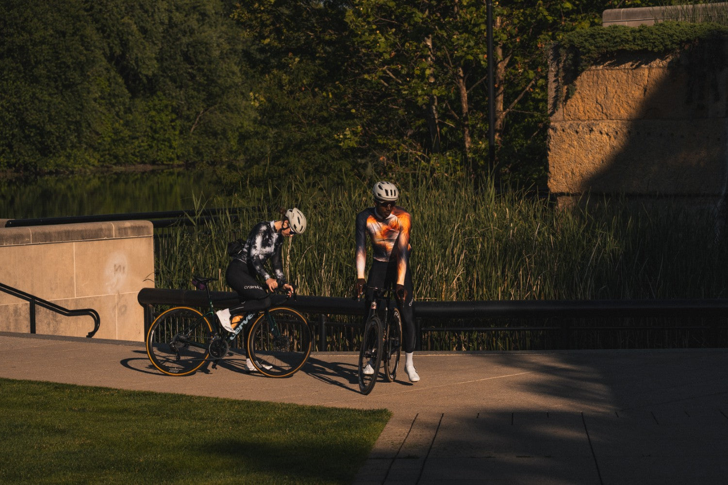 Two cyclists on a path with trees and a stone wall in the background