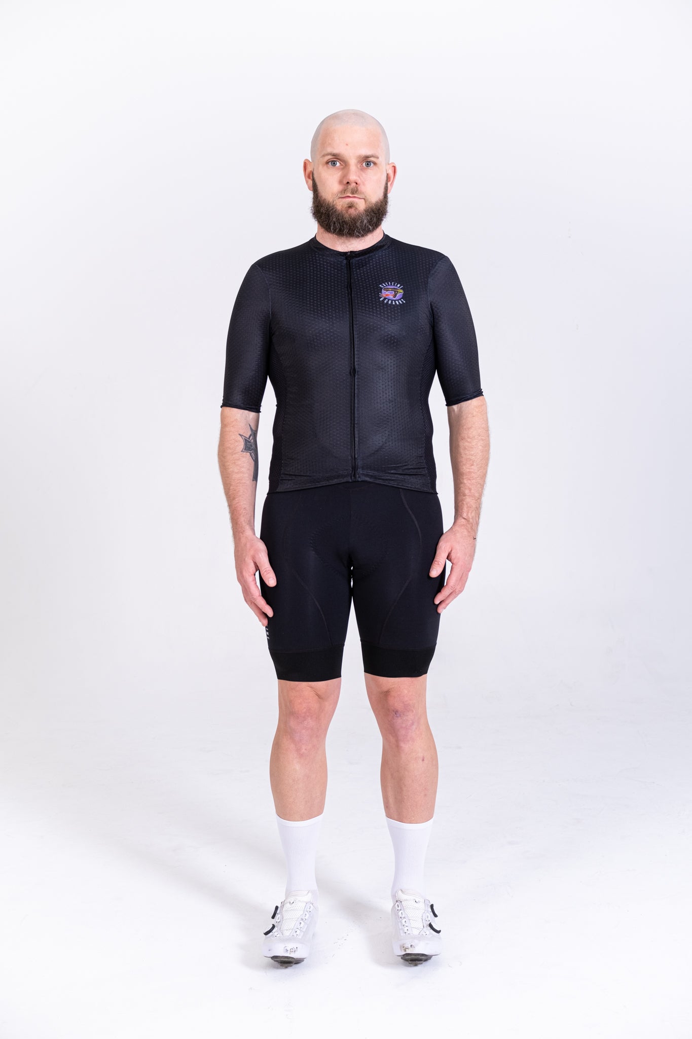 Full-body shot of a man in a black C&C Tattoo Series Skull cycling jersey & black shorts.