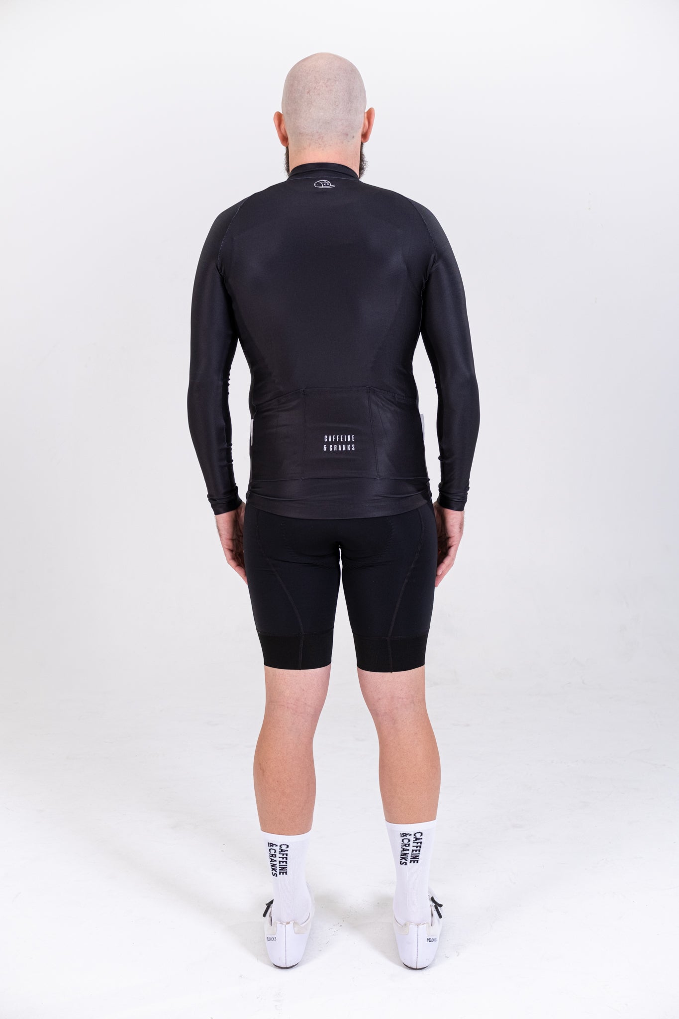 Back view of men's black long-sleeve thermal cycling jersey with pockets & black shorts.