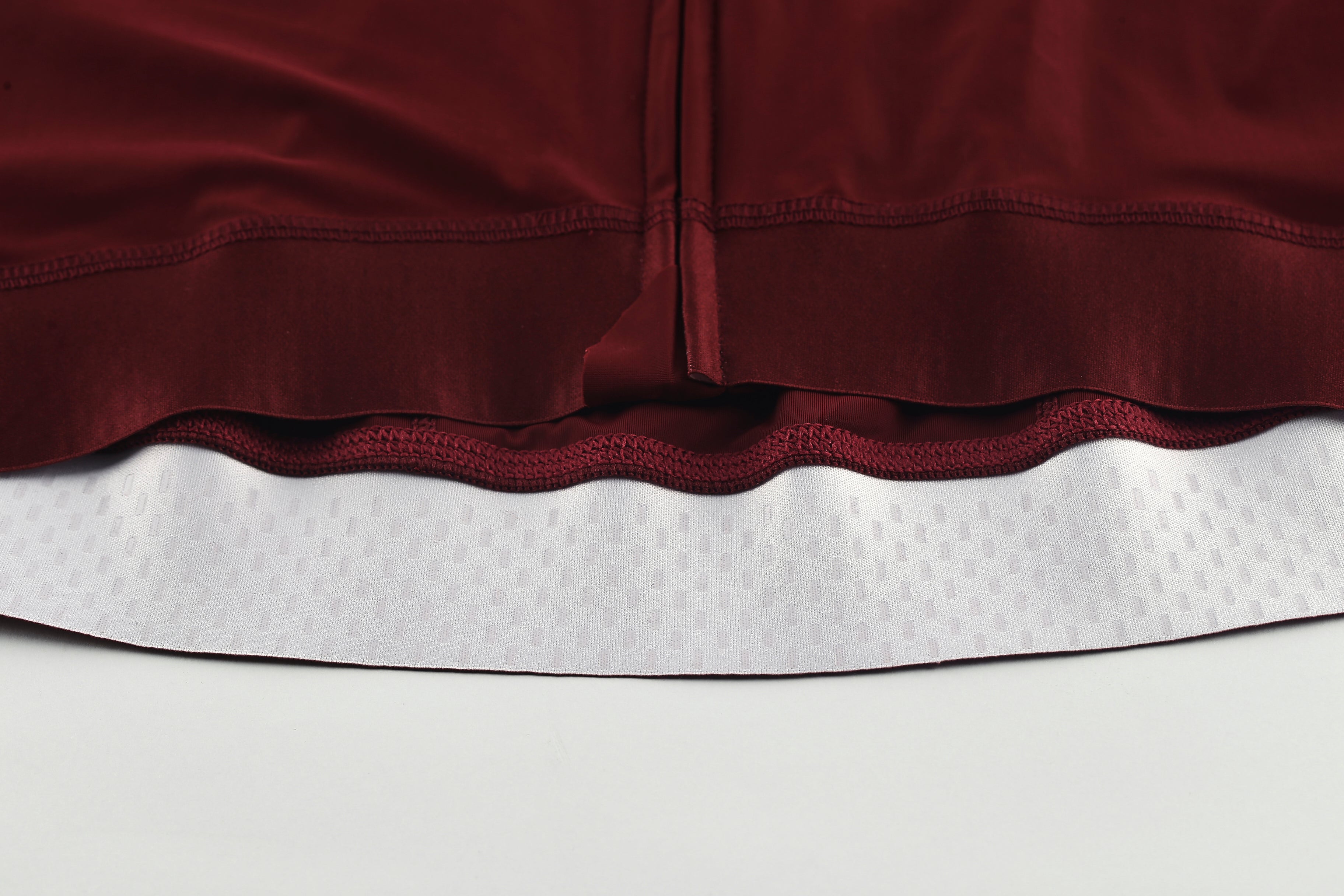 Close-up of Pinnacle Mens jersey hem in wine red, showing white textured gripper band.