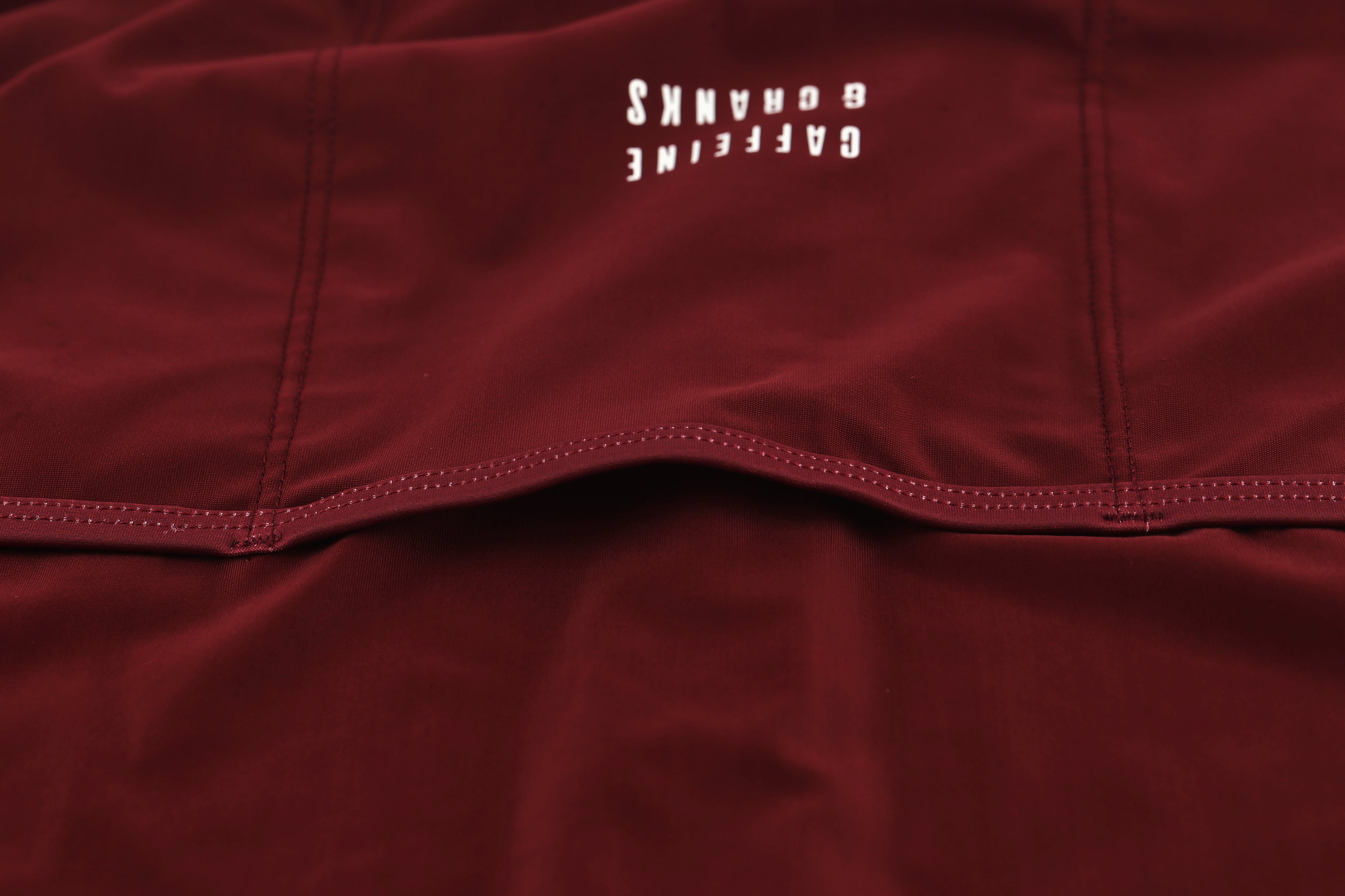 Close-up of a wine red men's jersey with white 'CAFFEINE & CRANKS' logo and white stitching detail.