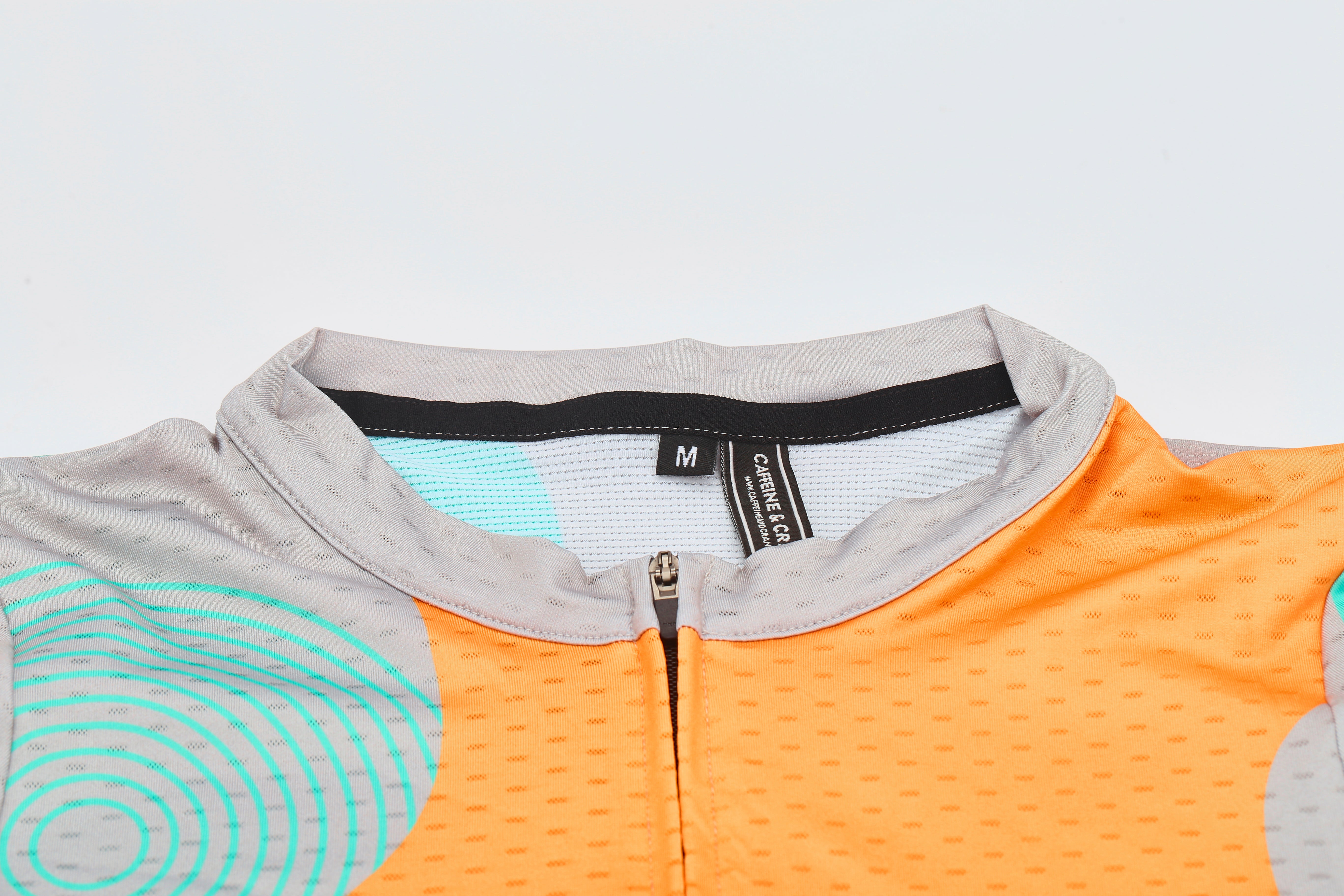 Close-up of C&C Memphis jersey collar, featuring orange & grey fabric, turquoise circles, and a silver zipper.
