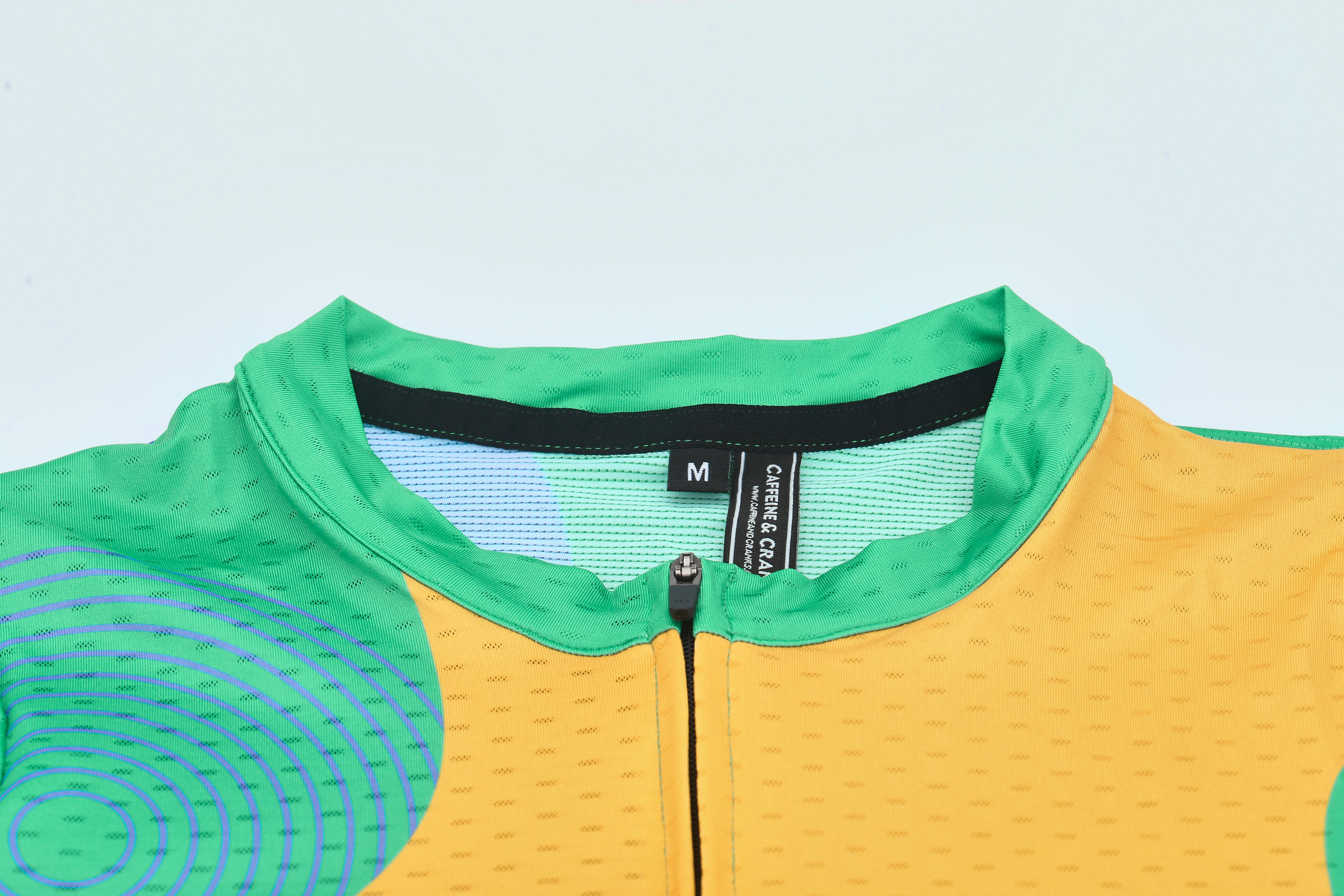 Close up of a women's C&C Memphis jersey with a green collar, orange front, and purple circular pattern.