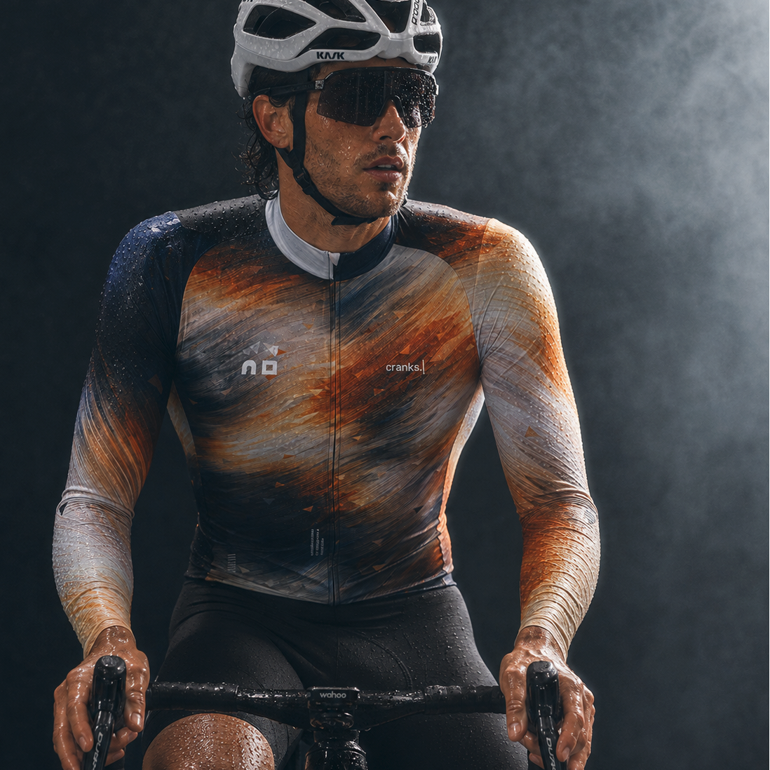 A cyclist wearing a long-sleeve cycling jersey with a galaxy nebula print, black shorts, a white and black helmet, and sunglasses, riding against a dark smoky background.